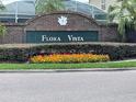 A brick community sign for Flora Vista, with well-maintained landscaping and colorful flowerbeds at 13016 Islamorada Dr, Orlando, FL 32837