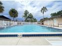 Community pool surrounded by palm trees and a white fence on a cloudy day with chair for lounging at 2316 E Margarita Ct, Kissimmee, FL 34741