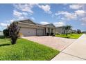 View of a single-story home featuring a brick driveway, lush green lawn, and a two-car garage at 2249 Palmetum Loop, Apopka, FL 32712