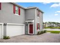 Gray two-story home featuring a white garage door, red door and shutters, and a brick driveway at 3039 Meleto Blvd, New Smyrna Beach, FL 32168