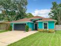 Charming turquoise home featuring a well-kept lawn, a dark grey garage door, and a cozy front porch at 2545 El Portal Ave, Sanford, FL 32773