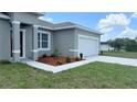 A close-up view of a well-maintained grey home with a white garage door and a landscaped garden at 3498 Sw 131St Place Rd, Ocala, FL 34473