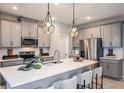 Modern kitchen features gray cabinetry, stainless steel appliances, pendant lighting, and an expansive white countertop island at 560 Southern Edge Way, Sanford, FL 32771