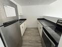 Galley kitchen featuring stainless steel refrigerator, light wood floors, white cabinets, and black countertops at 7604 Forest City Rd # 11, Orlando, FL 32810