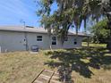 Rear exterior view of house showing windows, gray exterior paint, covered patio and large shade tree in the backyard at 141 W G H Washington St, Apopka, FL 32703
