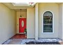 Close-up of the front door with red paint, an oval glass window, and a decorative light fixture at 602 Nighthawk Cir, Winter Springs, FL 32708