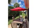 Outdoor patio with a dining table under a red umbrella, surrounded by greenery and landscaping at 1121 Alcove Loop, The Villages, FL 32162
