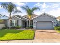 Inviting single-story home with a well-manicured lawn, brick driveway, and lush palm trees under a clear blue sky at 3925 Green Sabal Dr, Orlando, FL 32824