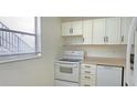 Galley kitchen features white cabinets and appliances with natural light from a window at 1504 Virginia Ave # 105, Daytona Beach, FL 32114