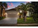 Charming single-Gathering home with a two-car garage, manicured lawn, and mature palm trees at dusk at 2506 Aster Cove Ln, Kissimmee, FL 34758