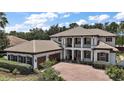Elegant two-story home with a tile roof, brick driveway, manicured landscaping, and a three-car garage at 5683 Bassett Pl, Sanford, FL 32771