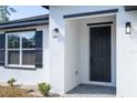 Close-up of a black front door with sidelights, complemented by a black frame window with shutters at 506 St Johns Ct, Poinciana, FL 34759