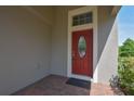 Close up of a red, oval-windowed front door with brick paver landing and grey exterior paint at 5908 Paxton Ct, Apopka, FL 32703
