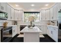Bright kitchen boasts white cabinetry, sleek black appliances, stone countertops, and center island beneath recessed lighting at 152 Riggings Way, Clermont, FL 34711