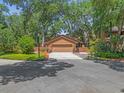 Exterior facade featuring mature trees, landscaping, & two car garage at 5 W Village Dr, Oviedo, FL 32765