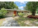 Quaint one-story home with mature trees, lush landscaping, and an inviting red front door at 17 S Aurora Dr, Apopka, FL 32703
