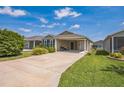 View of the house highlighting the driveway leading to the covered carport, with a well manicured lawn at 747 Louise Ln, The Villages, FL 32163