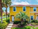 Bright yellow townhome featuring lush tropical landscaping and red tile roof, offering charming curb appeal at 3002 Secret Lake Dr, Kissimmee, FL 34747