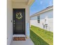 Inviting front entrance with a stylish black door, floral wreath, 'Welcome' sign, and 'hello spring' doormat at 4122 Sagefield Dr, St Cloud, FL 34773