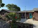 Charming brown home featuring a turquoise door and lush landscaping with vibrant plants and a red hibiscus at 11314 Huggins St, Leesburg, FL 34788