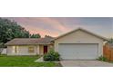 Inviting single-story home featuring a two-car garage, red front door, and manicured green lawn at dusk at 10739 Lake Ralph Dr, Clermont, FL 34711