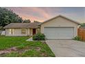 Well-kept single-story home with an attached two-car garage and a vibrant red door, set against a colorful sky at 10739 Lake Ralph Dr, Clermont, FL 34711