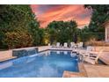 A beautiful backyard pool with a tranquil waterfall, lounge chairs, and lush landscaping against a colorful sunset backdrop at 1420 Palmer Ave, Winter Park, FL 32789