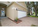 View of the two-car garage with a brick paver driveway and neatly landscaped features at 2306 Valhalla Dr, Tavares, FL 32778