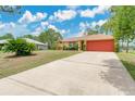 A large concrete driveway leads to a tan home with red garage doors, contrasting well with the clear blue sky at 2772 Pelham Cir, Deltona, FL 32738