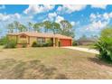 A tan, one-story home features a red garage door and landscaping. Grass yard shows evidence of drought at 2772 Pelham Cir, Deltona, FL 32738