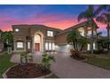 Grand two-story home featuring a brick driveway, arched entry, and lush tropical landscaping at twilight at 2828 Northampton Ave, Orlando, FL 32828