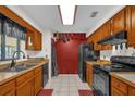 Well-lit kitchen with wooden cabinets, black appliances, tile flooring and red accent wall at 1588 Alloway Dr, Deltona, FL 32738