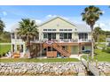 View of the rear exterior featuring a wooden deck, stairs to the water, and mature landscaping at 291 River Rd, Oak Hill, FL 32759