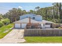 View of a two-car garage, fenced in backyard, and grassy area with mature trees and a sunny sky above at 1601 Randolph St, Deltona, FL 32725