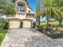 View of a stately two-story house with a balcony, two-car garage, brick driveway and tropical landscaping at 16246 Ravenna Ct, Montverde, FL 34756
