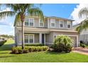 Two-story gray home with a well-maintained lawn, tropical landscaping, and a brick driveway to the attached garage at 2431 Tudor Rose Dr, Sanford, FL 32773