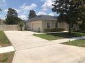 View of a tan single-story home featuring an attached garage, a long driveway, and manicured landscaping at 2555 Palmetto Ridge Cir, Apopka, FL 32712