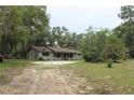 Ranch-style home featuring a long covered front porch, gravel driveway, mature trees, and natural landscaping at 26586 Se Highway 42, Umatilla, FL 32784