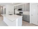 Modern kitchen featuring stainless steel appliances, quartz countertops, and gray cabinets, offering a sleek design at 9112 Wildlight Trl, Wildwood, FL 34785