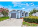 Charming home featuring light blue siding, a gray garage door, landscaped yard with vibrant flowers, and concrete driveway at 104 Yorktown Pl, Sanford, FL 32771