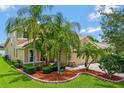 Landscaped front yard with palms and manicured bushes leading to a tan two-story home with a tile roof and paver driveway at 2631 Captains Ct, Kissimmee, FL 34746