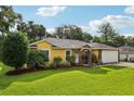 Charming yellow house featuring a well-manicured lawn, lovely landscaping, and an attached two-car garage at 395 Alcazar Ave, De Leon Springs, FL 32130