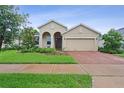 Charming beige home with a brick driveway, a cozy arched entryway, and lush green landscaping at 2339 Jernigan Loop, Kissimmee, FL 34746