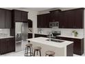 Modern kitchen featuring dark cabinets, stainless steel appliances, a white countertop island, and bar stool seating at 3021 Namaste Dr, Clermont, FL 34714