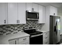 Close-up of kitchen with white cabinets, stainless steel appliances, and mosaic backsplash at 508 Bennett St, Auburndale, FL 33823