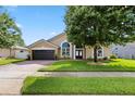 Inviting tan home with a dark garage door, arched windows, and lush green lawn at 1008 Soldier Creek Ct, Oviedo, FL 32765
