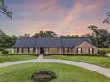Charming brick home with a circular driveway, lush green lawn, and mature landscaping at dusk at 104 Amberwood Ct, Longwood, FL 32779