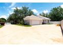 Wide angle view of light colored home with large driveway, manicured bushes and mature trees under blue skies at 1586 Antoinette Ct, Oviedo, FL 32765