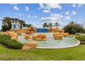 Beautiful rock water fountain with palm trees, lush landscaping, and a clear blue sky at 9844 Beach Port Dr, Winter Garden, FL 34787