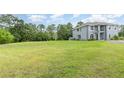 Spacious grassy side yard of a grey stucco home with mature trees in the background under a sunny sky at 32125 Wekiva Pines Blvd, Sorrento, FL 32776